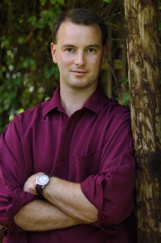 Andrew Daldorph wearing a purple shirt, leaning against a tree.
